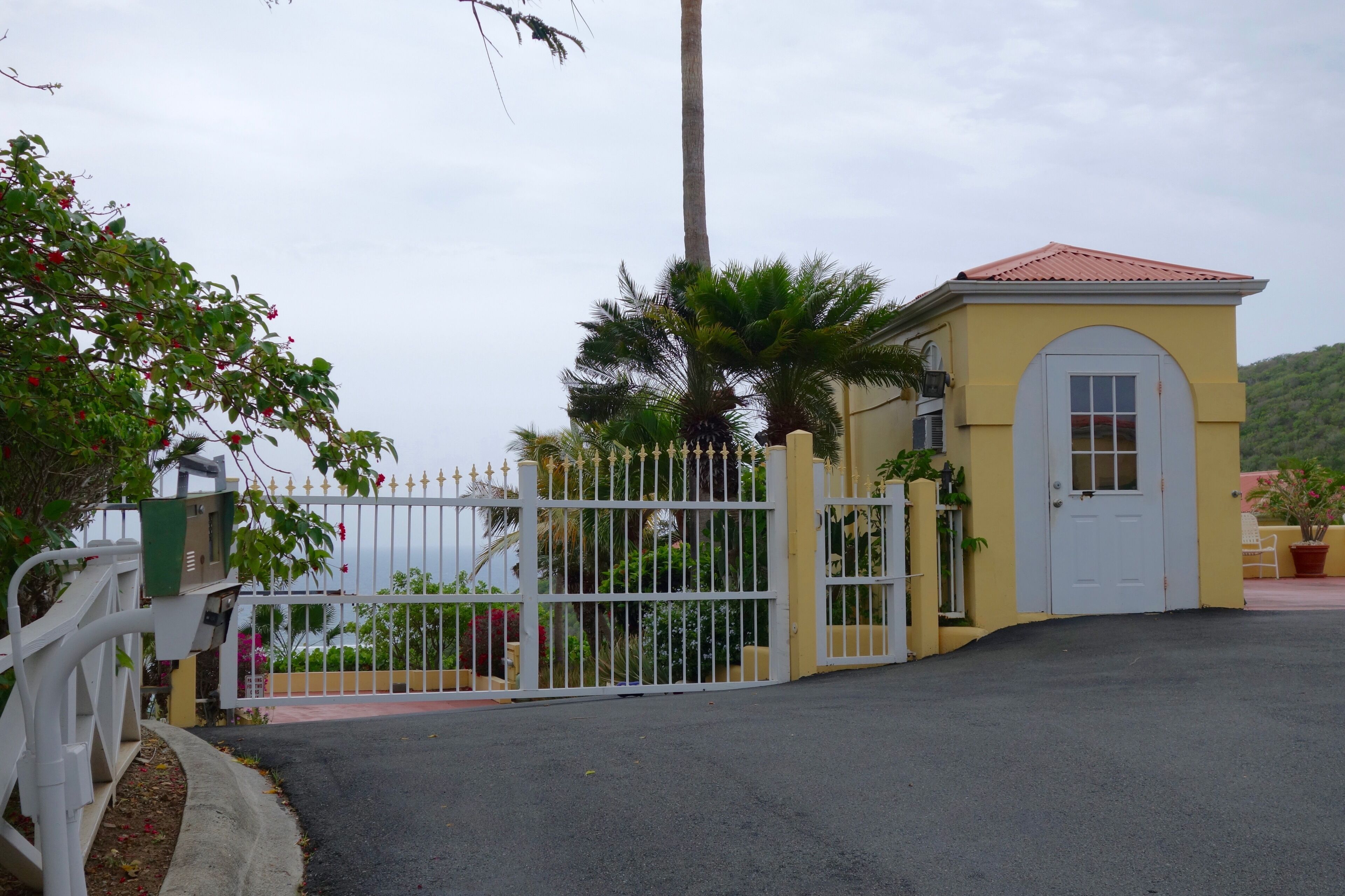 A gated entrance with a yellow building, a white door, and a white fence.