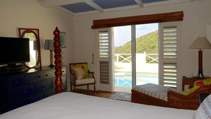 Une chambre à coucher comprenant un lit, une télévision, une chaise, une lampe et donnant sur une piscine et des collines.