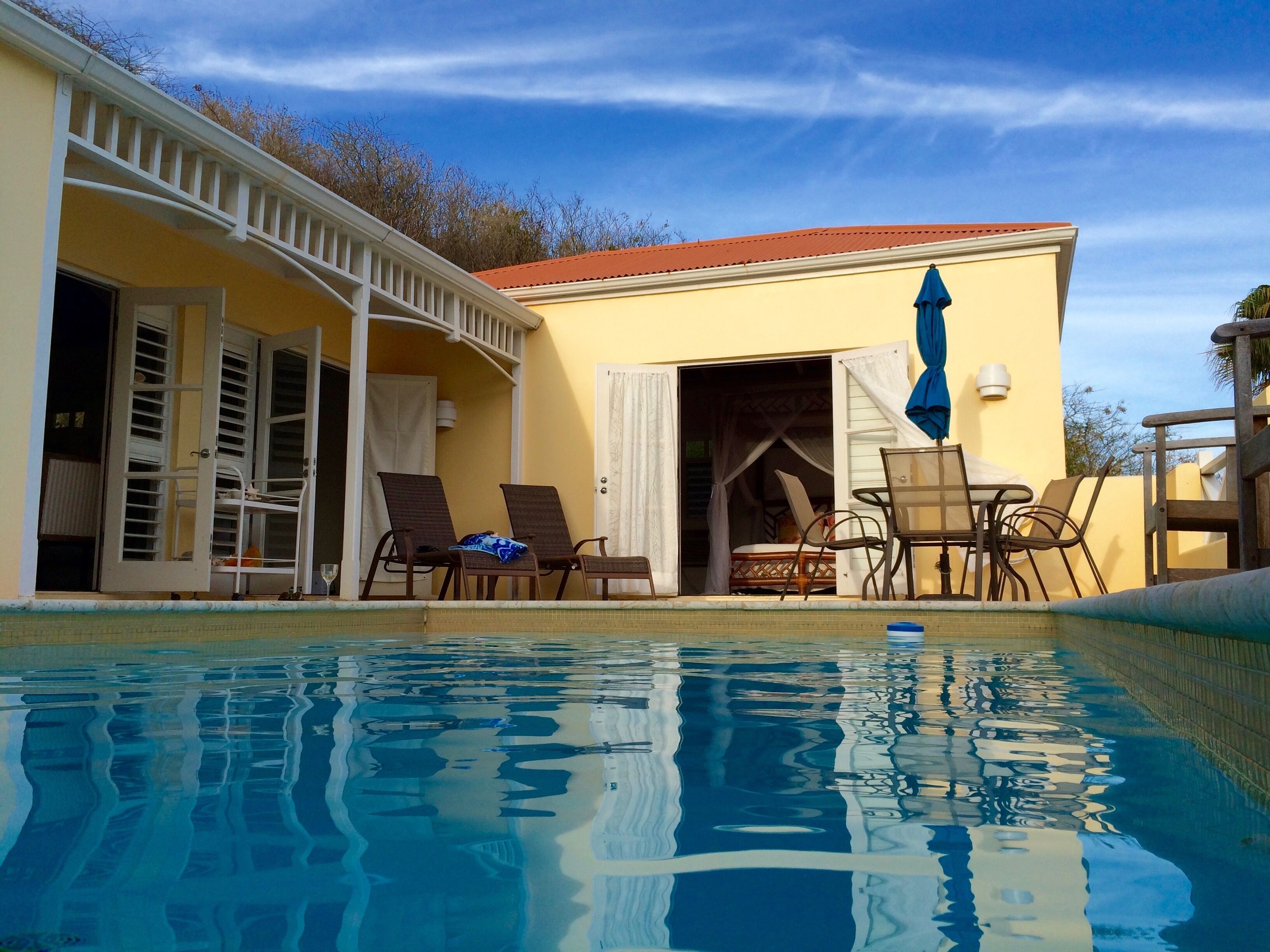 A poolside area with a yellow building, white railings, and a red roof.