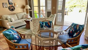 Un salon avec une table basse en verre, entouré de fauteuils en osier, d’un canapé et d’un fauteuil à motifs.