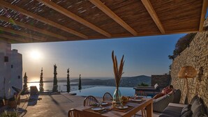 Un comedor con vista al mar, muebles de madera y paredes de piedra.