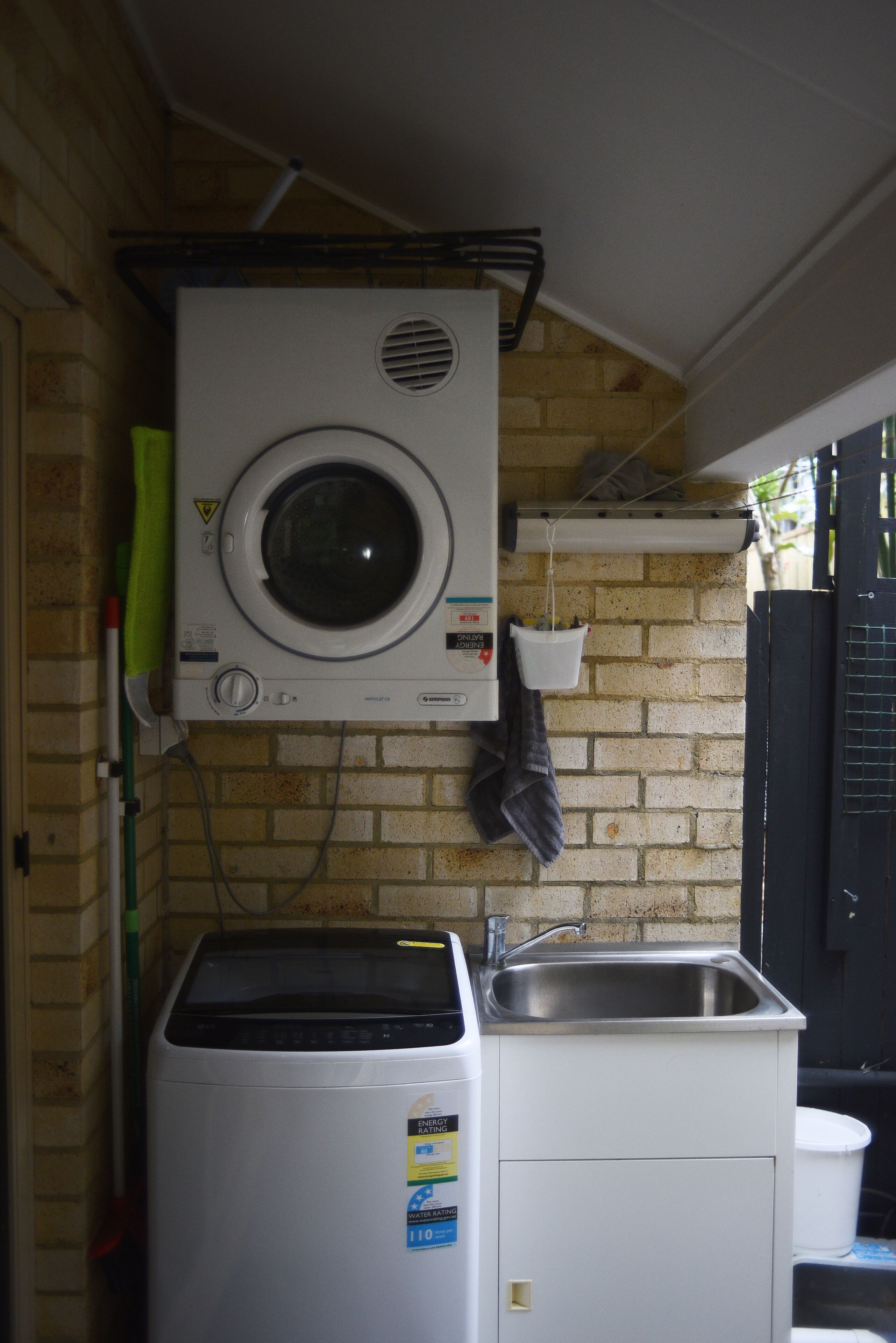A compact laundry area with a washing machine and a built-in dryer, a sink, and a hanging rack.