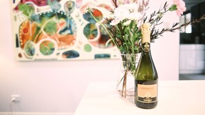 A bottle of Prosecco San Ginesco wine and a vase with flowers on a table.
