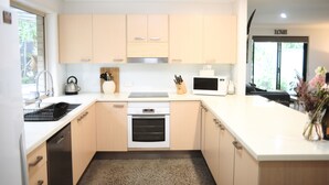 A modern kitchen with light wood cabinets, a stainless steel oven, a dishwasher, and a microwave.