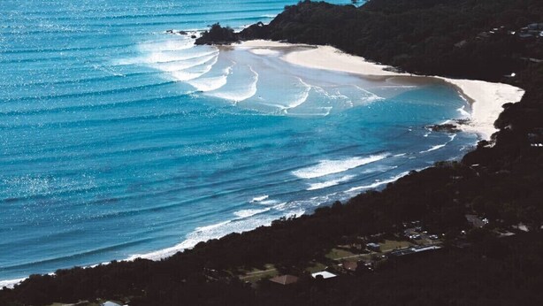 A coastal landscape with a beach, ocean waves, and a distant shoreline.