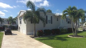 A single-story mobile home with a paved driveway, surrounded by well-maintained grass and palm trees. - Beautiful Home in Ft Myers Beach. (Fort Myers Beach)