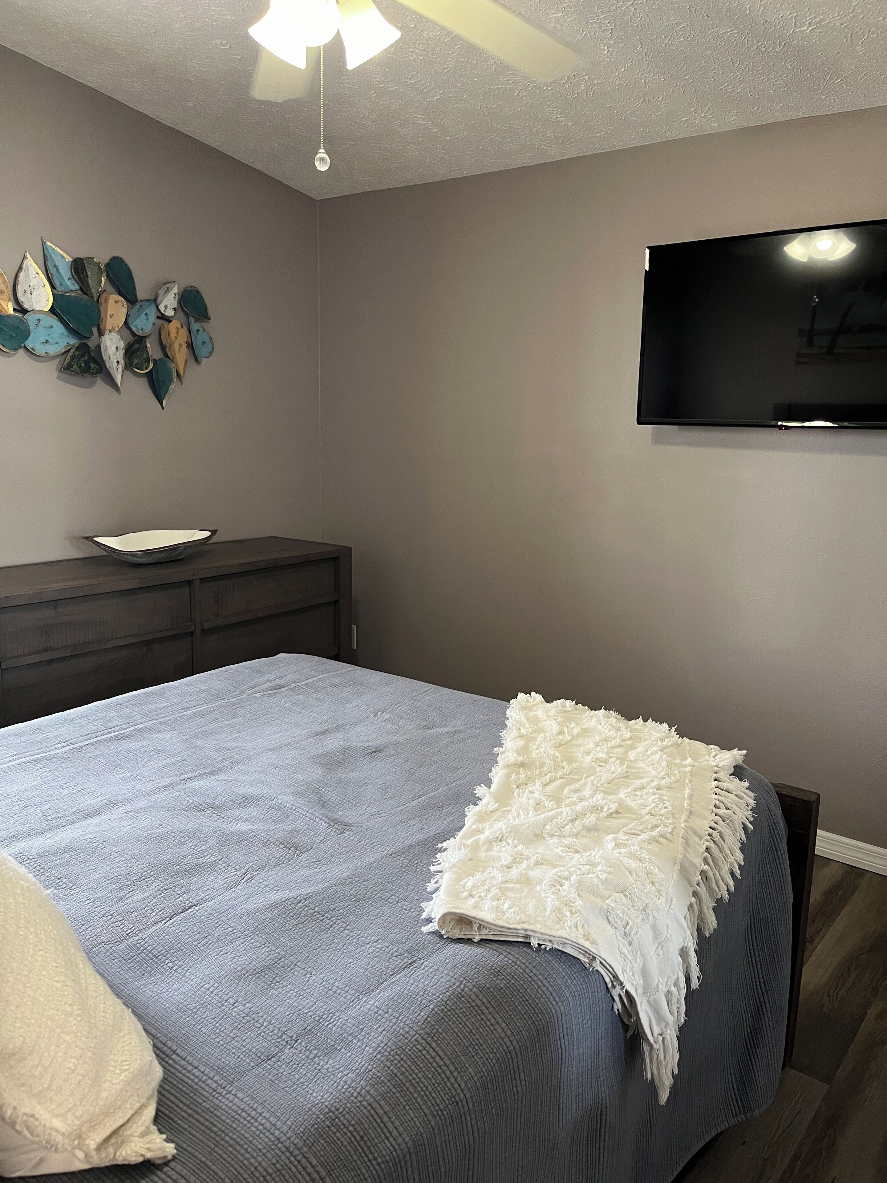 Una camera da letto con un letto, una cassettiera, una televisione a schermo piatto e un elemento decorativo a parete.