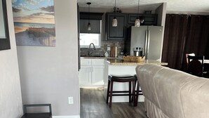 A modern living room with a sofa, a coffee table, and a rug. There is a kitchen area in the background with cabinets and a countertop. - Beautiful Home in Ft Myers Beach. (Fort Myers Beach)