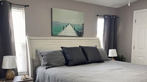 A bedroom with a bed, nightstands, a ceiling fan, a painting, and a view of the outdoors. - Beautiful Home in Ft Myers Beach. (Fort Myers Beach)