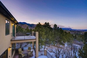 A two-story building with a balcony, outdoor seating, and a view of mountains.