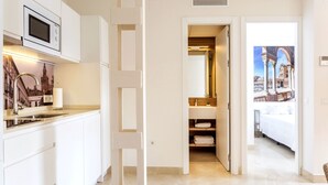 Une chambre d’hôtel moderne dotée d’un coin cuisine, d’une salle de bain avec un grand miroir et d’un lit orné d’une fresque représentant un paysage urbain.