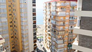 Un edificio de gran altura con múltiples balcones, un estacionamiento al frente y vista a la playa.