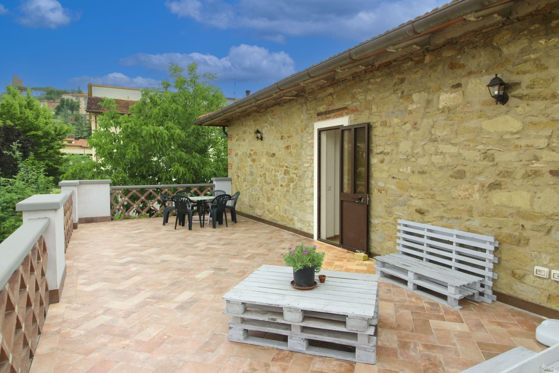 A stone building with a door, a small table with a potted plant, and two benches.
