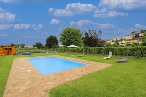 A rectangular swimming pool with a herringbone tile border, surrounded by a grassy lawn with lounge chairs.
