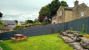 Un patio trasero con una mesa de picnic de madera, un muro de piedra y una valla de madera.