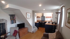 Una sala de estar con sofá, televisor, estantería y una escalera que lleva a una zona de cocina con estufa y lavaplatos.