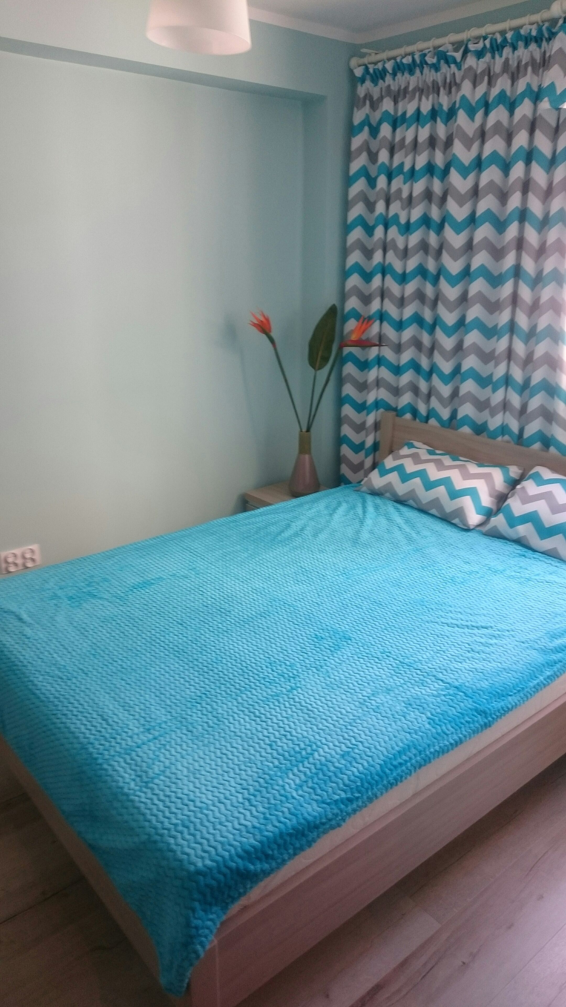 A bedroom with a bed, a nightstand, a vase with flowers, and a window with curtains.