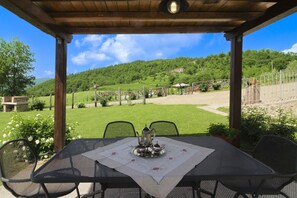 A covered outdoor seating area with a table set for two, overlooking a green landscape with hills and a clear sky. - Beautiful private villa for 7 people with private pool and TV (Città Di Castello)