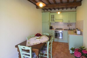 A kitchen with light green cabinets, a wooden table with a floral tablecloth, and a vase of red roses. - Beautiful private villa for 7 people with private pool and TV (Città Di Castello)