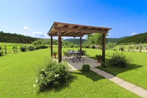 A covered outdoor seating area with a table and chairs, surrounded by a well-maintained lawn and garden. - Beautiful private villa for 7 people with private pool and TV (Città Di Castello)