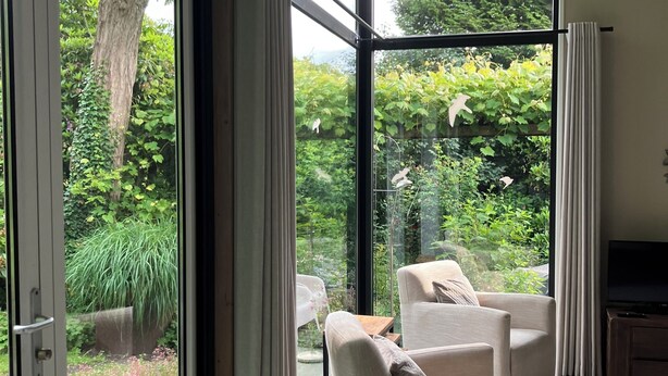 Un salon moderne doté d’une grande porte vitrée donnant sur un jardin, d’un canapé beige et d’une plante en pot.