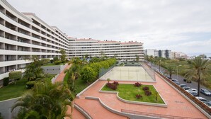 Un hotel de varios pisos con un patio que cuenta con cancha de tenis, palmeras y un jardín ajardinado.