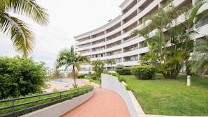 Un sendero curvo que conduce a un hotel de varios pisos con balcones, rodeado de vegetación y palmeras.