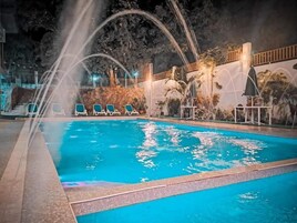 A swimming pool with water jets, surrounded by lounge chairs and palm trees.