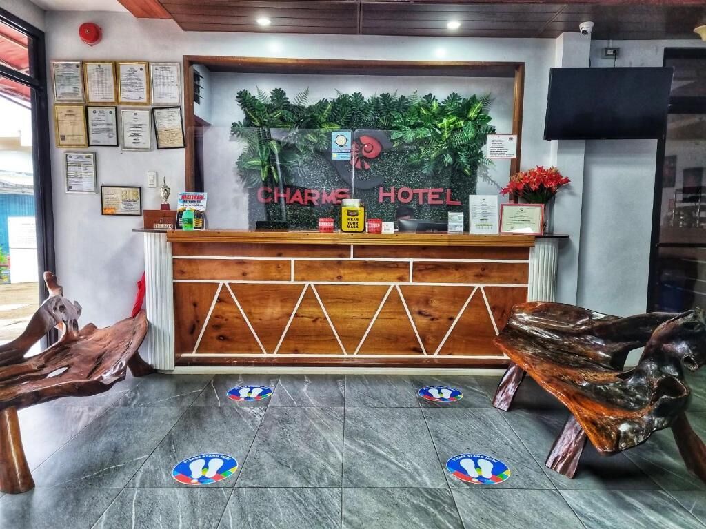 En receptionsdisk med en träbeklädd bardisk, inramade diplom och en skylt med texten ”CHARME HOTEL”.