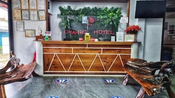 Un mostrador de recepción con encimera de madera, marcos con diplomas y un cartel que dice 'CHARME HOTEL'.