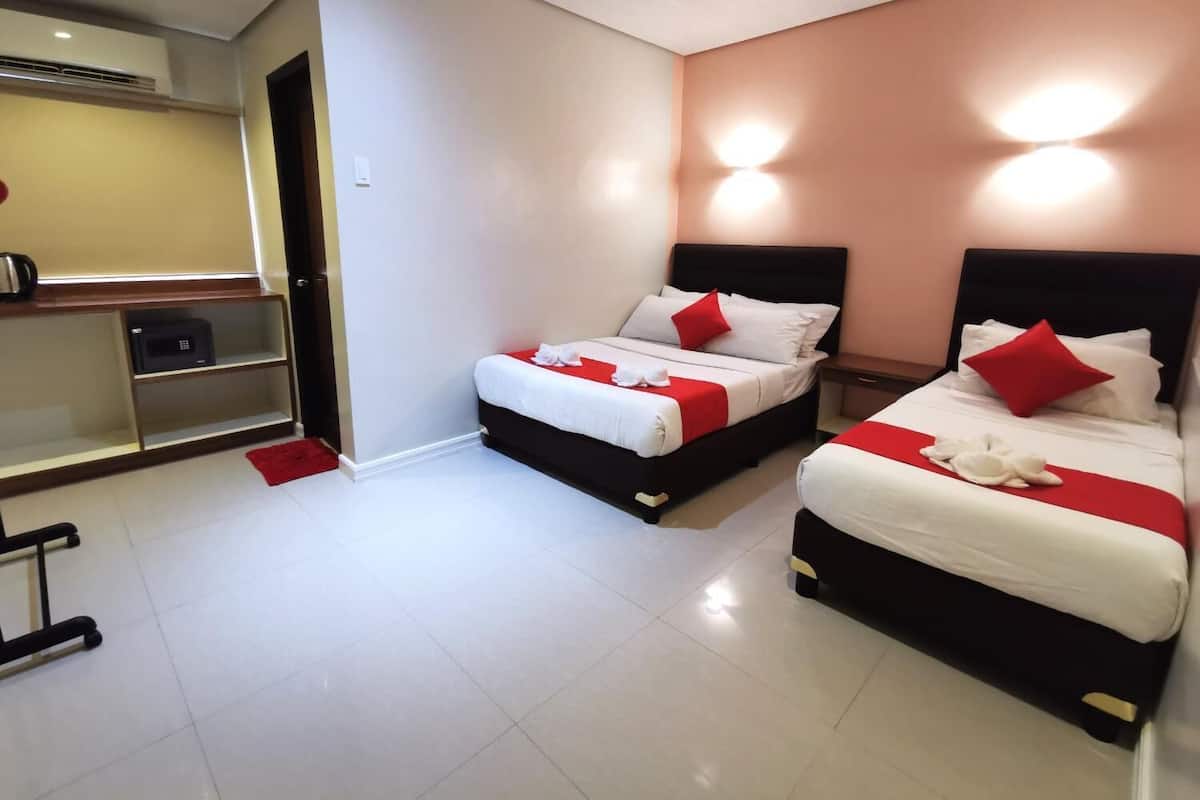 A hotel room with two beds, each with white bedding and red pillows, and a small seating area with a microwave.