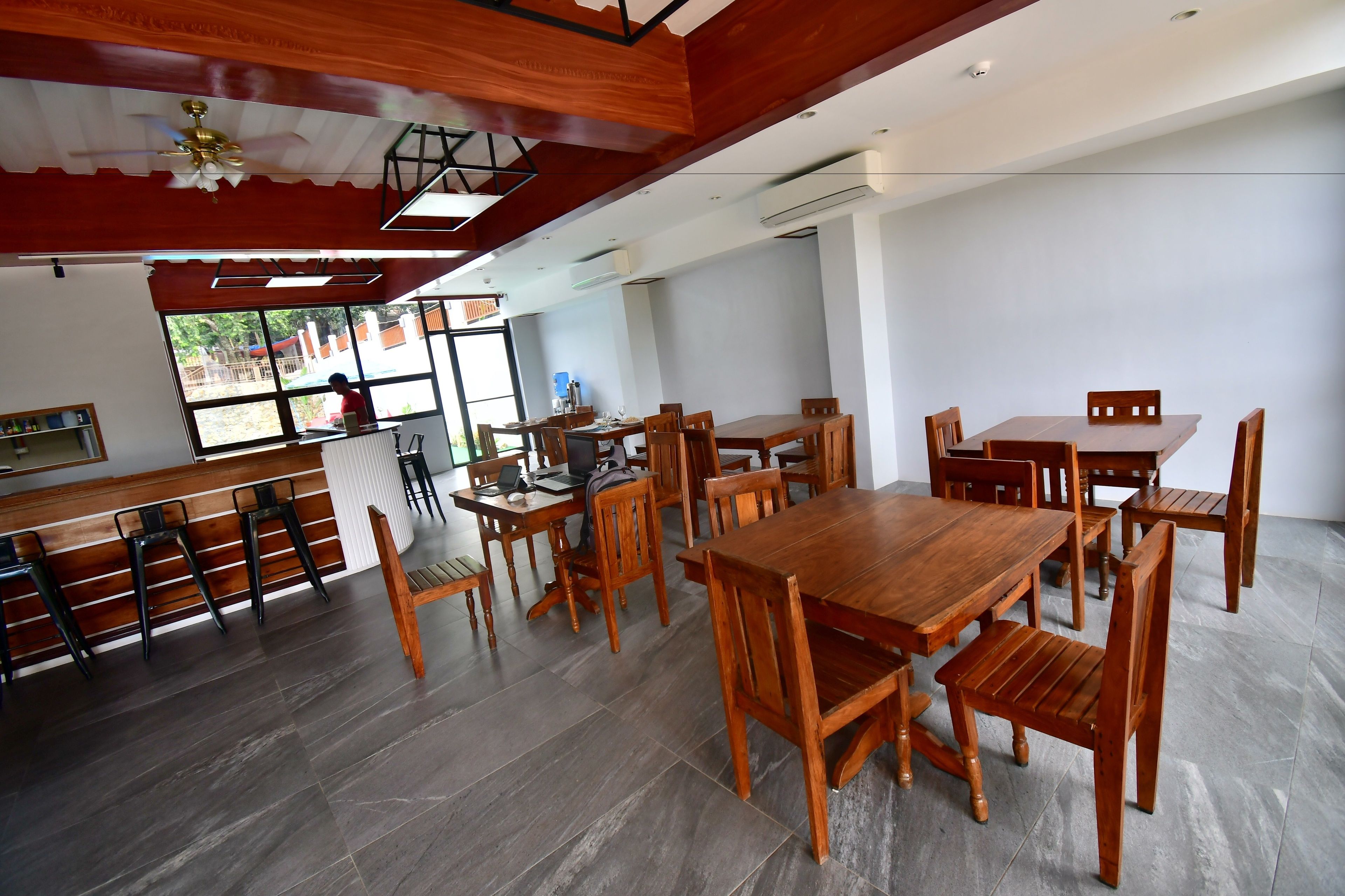 A spacious dining area with wooden tables and chairs, a bar area with stools, and a large window providing a view of the outside.