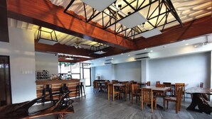 A spacious dining area with wooden tables and chairs, a bar area with a counter, and a high ceiling with exposed beams. - Charms Hotel (Coron)