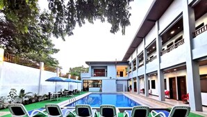 A pool area with lounge chairs and umbrellas, surrounded by a building with multiple balconies. - Charms Hotel (Coron)