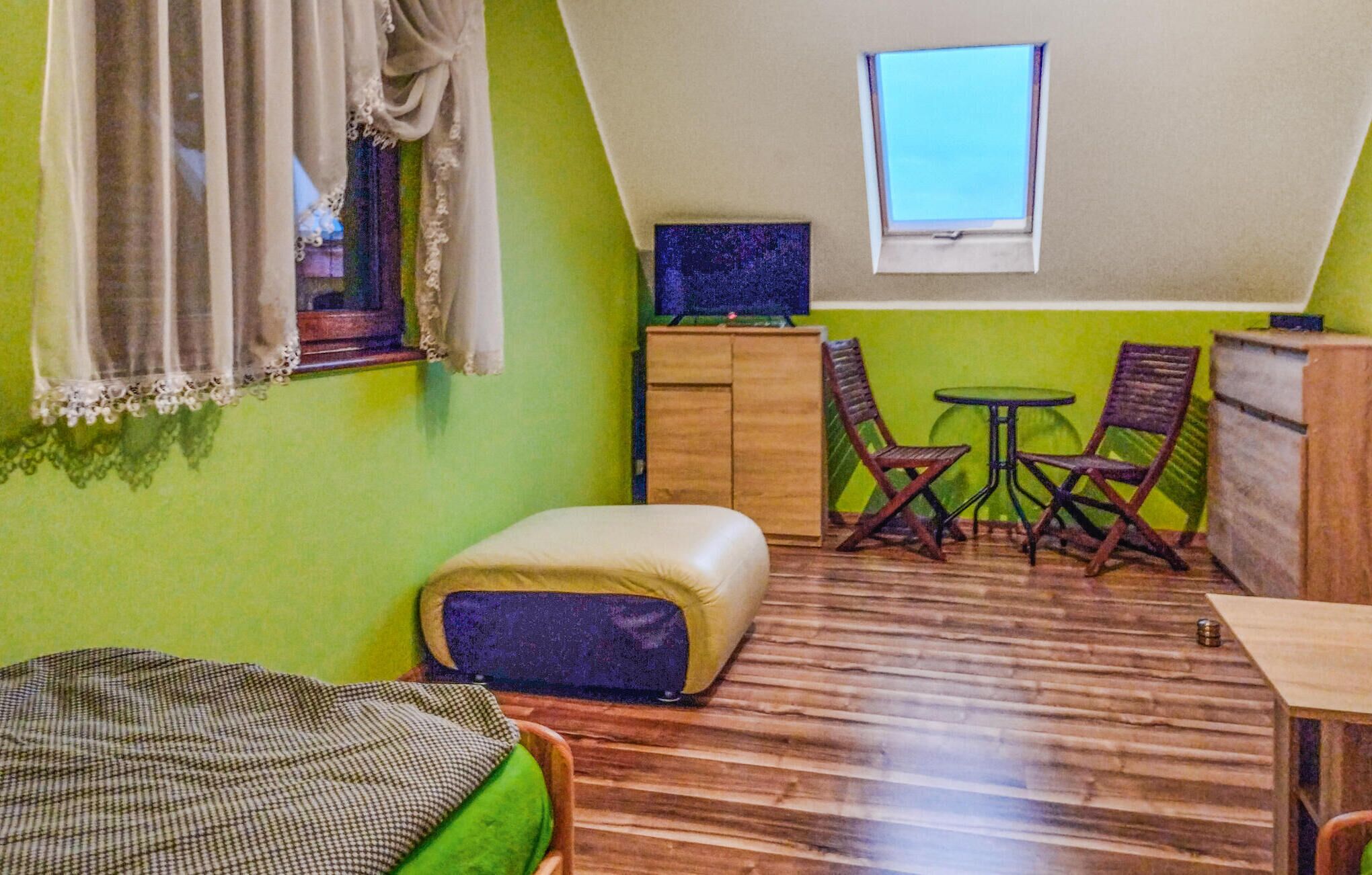 Une petite pièce agréable, avec un plafond en pente, un lit, une petite table avec des chaises et une fenêtre.