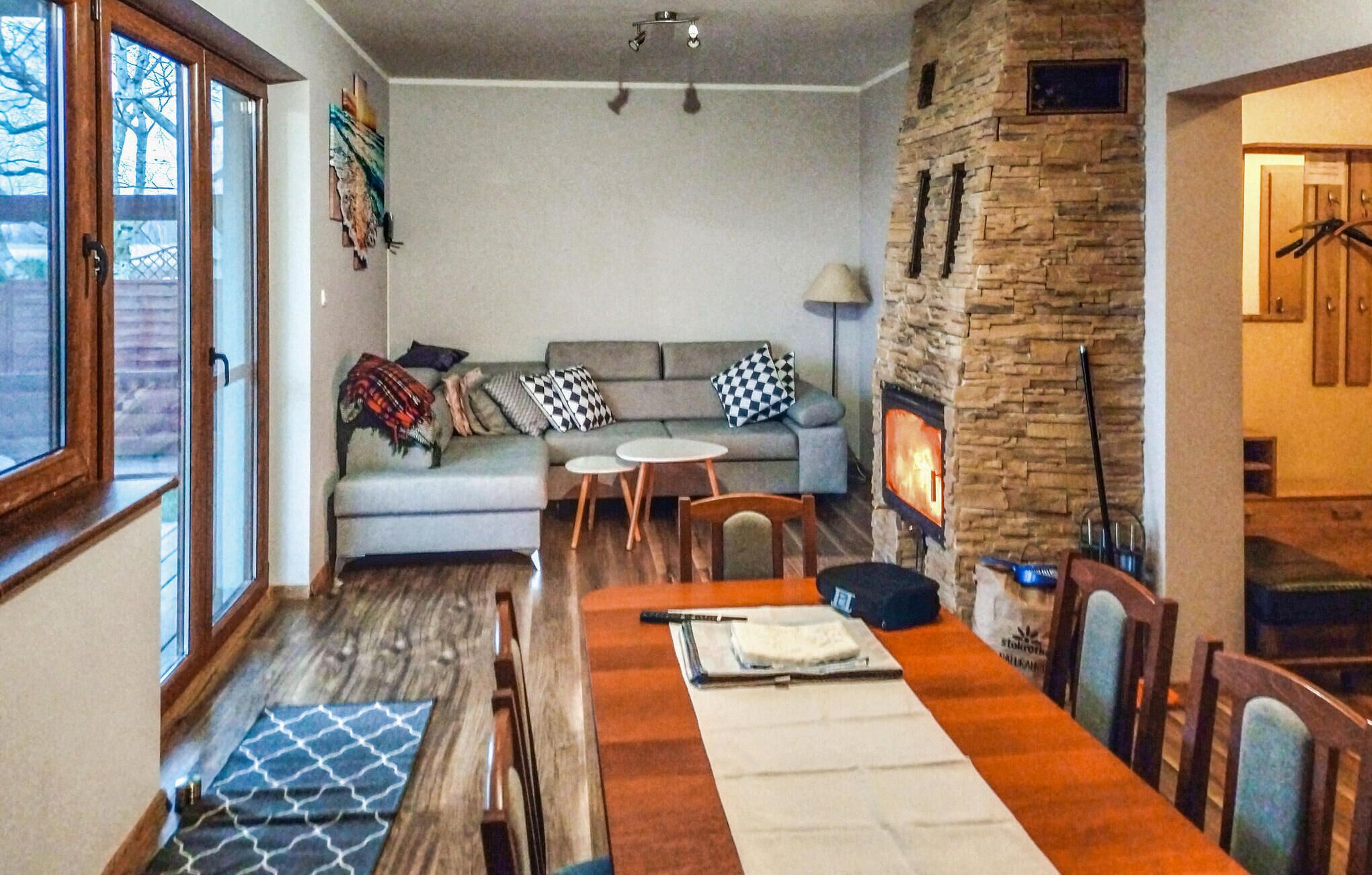 Un salon chaleureux avec une cheminée en pierre, un coin repas avec une table en bois et un canapé agrémenté de coussins à motifs.