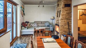 Ein gemütliches Wohnzimmer mit Kamin aus Stein, einem Essbereich mit Holztisch und einer Couch mit gemusterten Kissen.