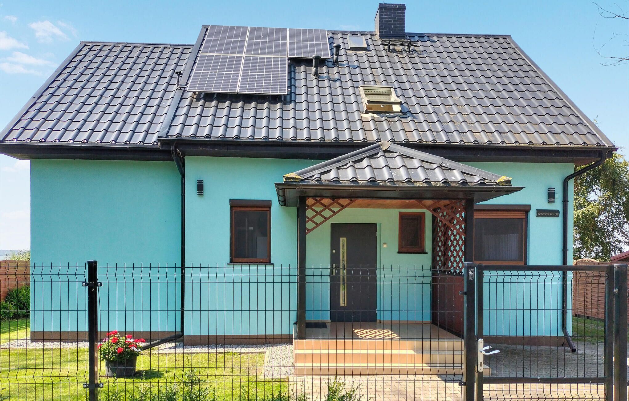 Une maison avec un toit en tuiles, des panneaux solaires et une cour clôturée.