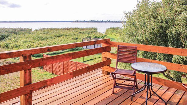 Eine Holzterrasse mit Tisch und Stühlen mit Blick auf ein Gewässer.