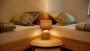 Una cama bien hecha con almohadas, una pequeña mesa de madera con una lámpara y una silla de madera.