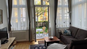 Ein Wohnzimmer mit einer Couch, einem Couchtisch, einem Fernseher und Blick ins Freie.