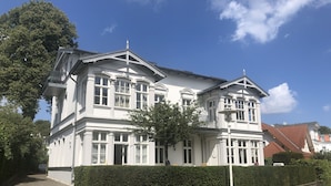 Ein großes, weißes Gebäude mit zwei Etagen, einer symmetrischen Fassade, zahlreichen Fenstern und einem markanten Balkon.