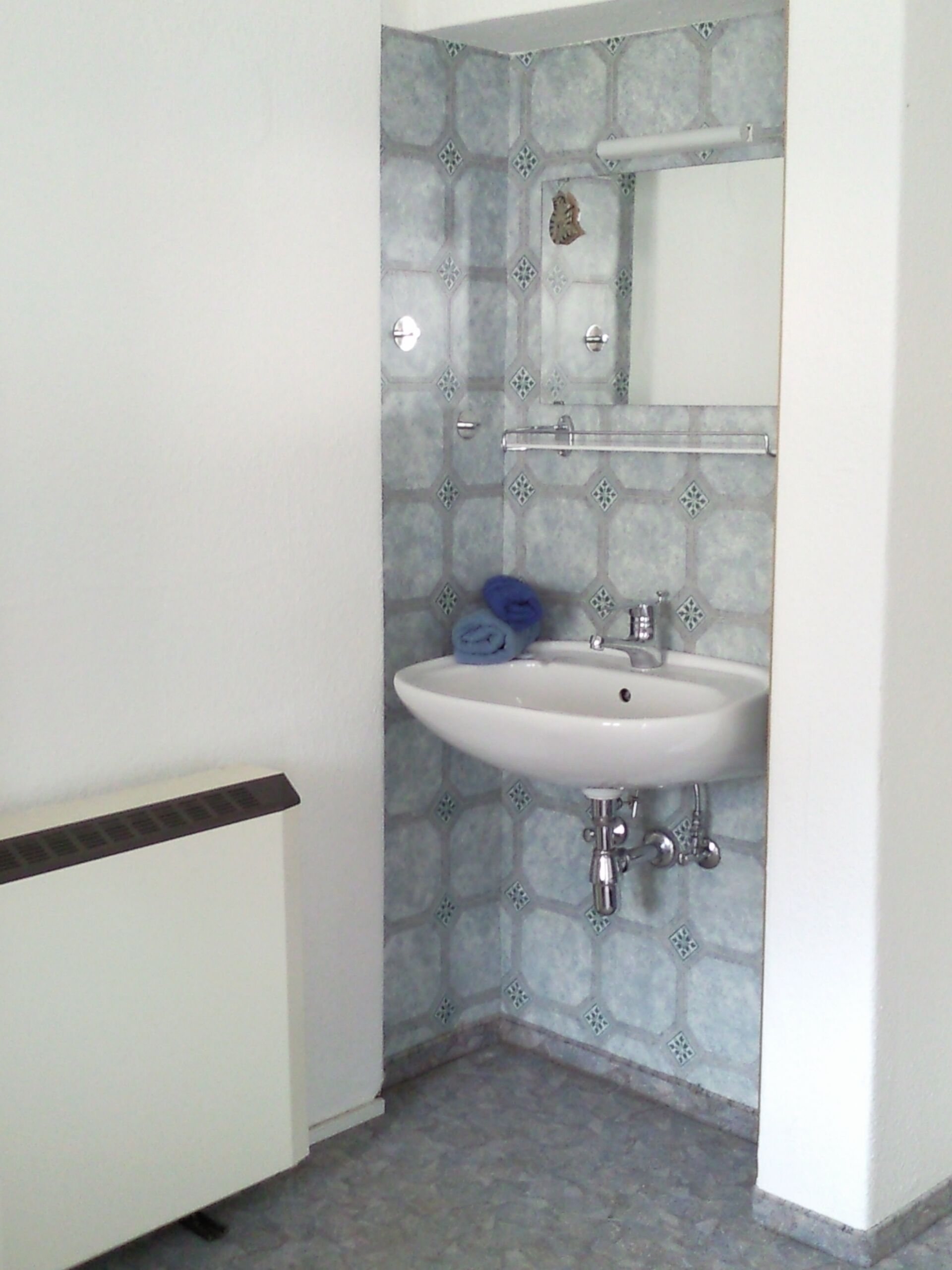 A bathroom with a white sink, blue towels, and a tiled backsplash.