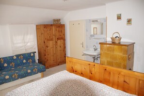 A bedroom with a wooden wardrobe, a bed with a floral bedspread, a wooden dresser with a mirror, and a window with white curtains. - Cozy cottage in a quiet location and wonderful views (Bad Gastein)