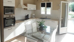 A modern kitchen with white cabinetry, a built-in microwave, a coffee maker, and a glass dining table with chairs. - Vaucluse- Pied du Ventoux- Le Barroux- Gravel house (Le Barroux)