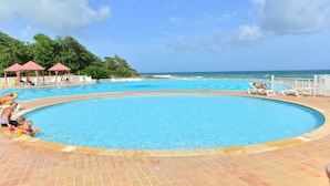 Una piscina con cubierta de baldosas, rodeada de sillones de descanso y sombrillas, con vistas al océano.