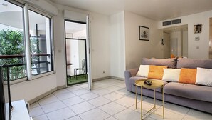 A modern living room with a grey sofa, a small round table, and a view through a sliding door to an outdoor balcony.