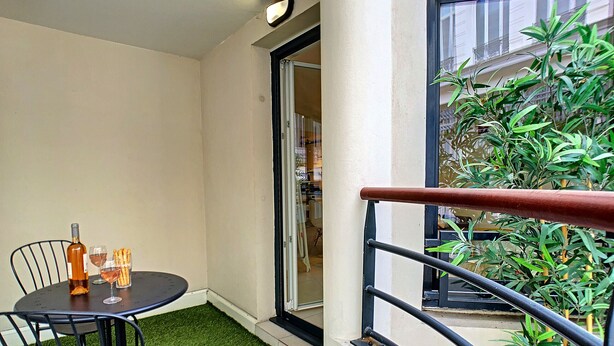 A balcony with a small table and chairs, a bottle of wine, and a glass.