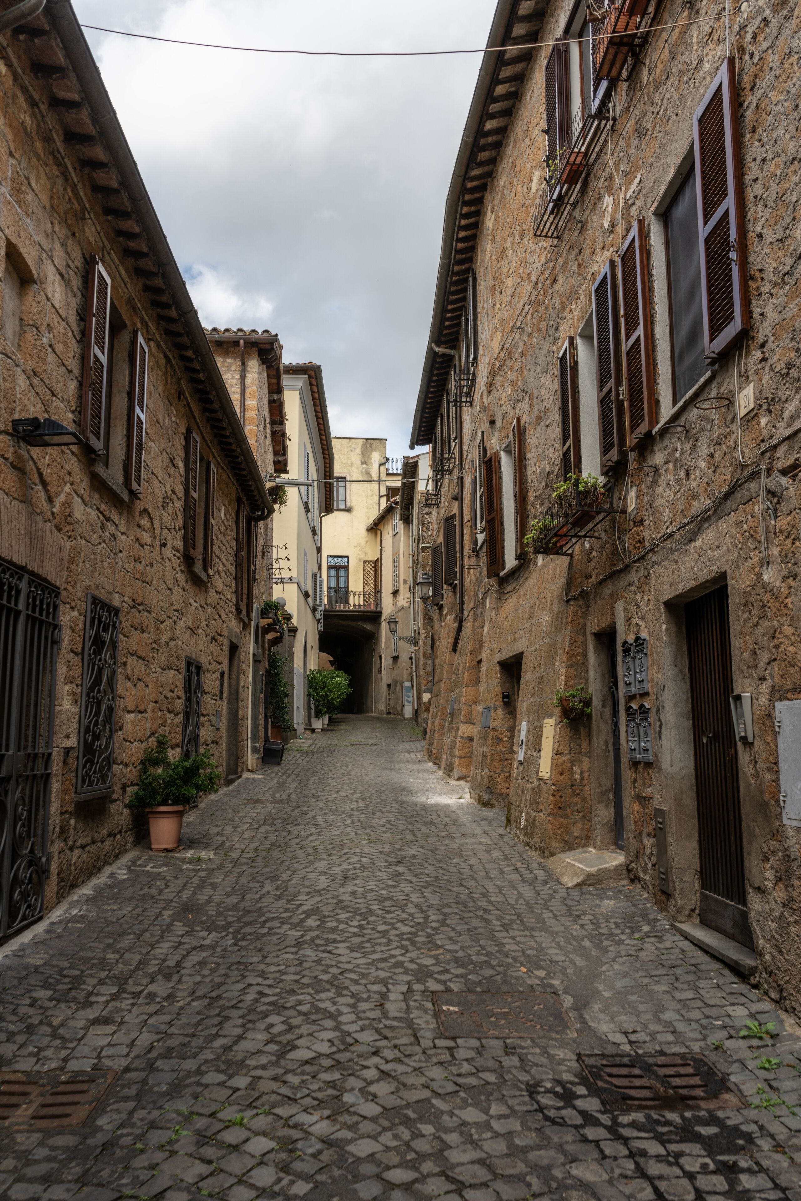 Une ruelle étroite pavée, bordée de bâtiments anciens en pierre, dotés de fenêtres grillagées et de balcons.