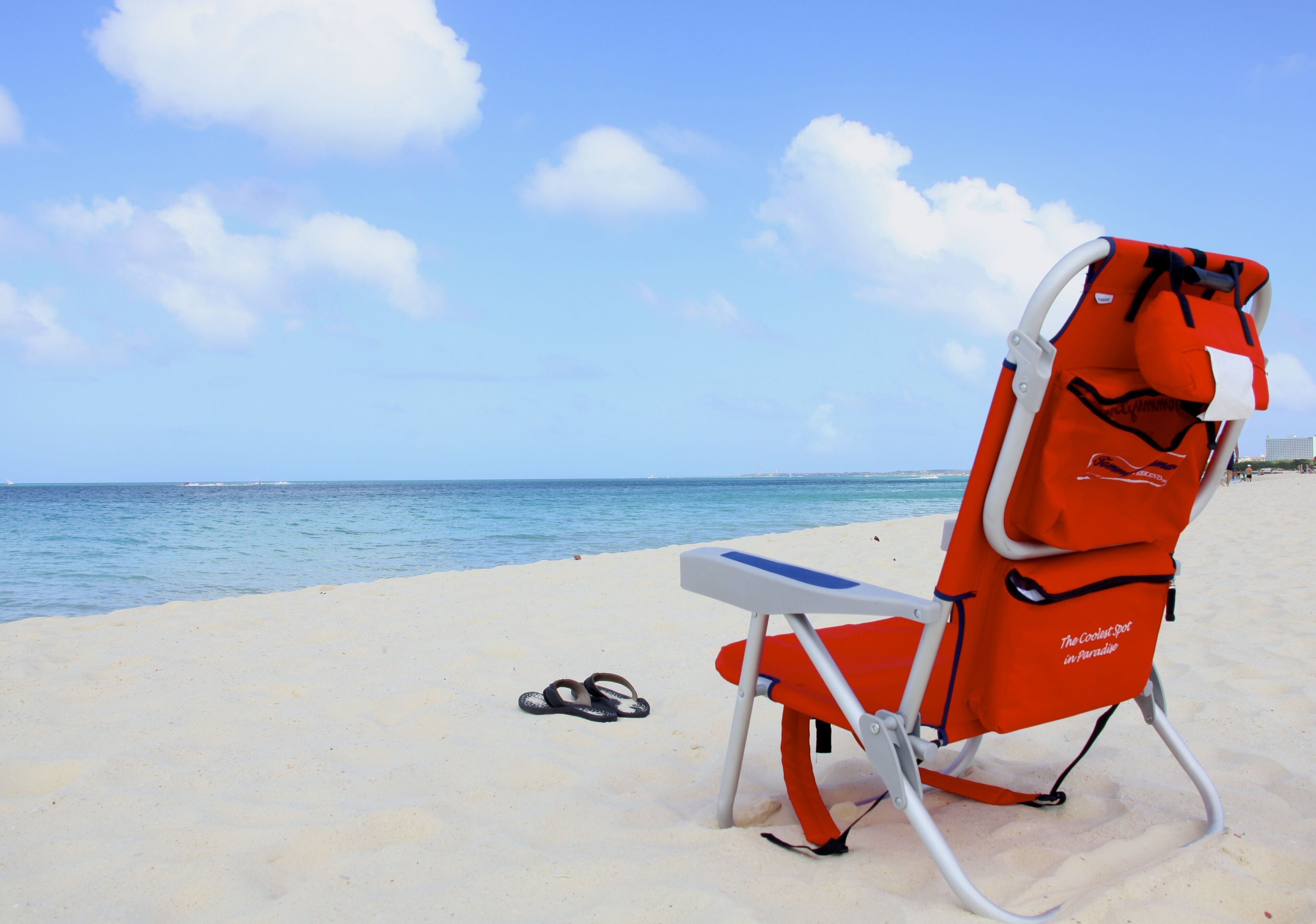A beach chair with a white and red design, placed on a sandy beach with a clear blue sky and calm sea in the background.